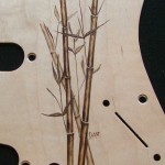 Close-up view of bamboo design woodburned on maple veneered aluminum pick guard - raw wood