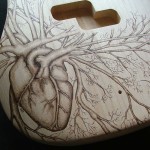 SOLD - Close-up view of human heart design woodburned on P bass guitar body - raw wood