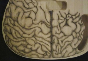 Close-up of human brain design woodburned on bass guitar body - raw wood.