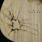 Close-up view of shattered glass design woodburned on guitar body - raw wood.